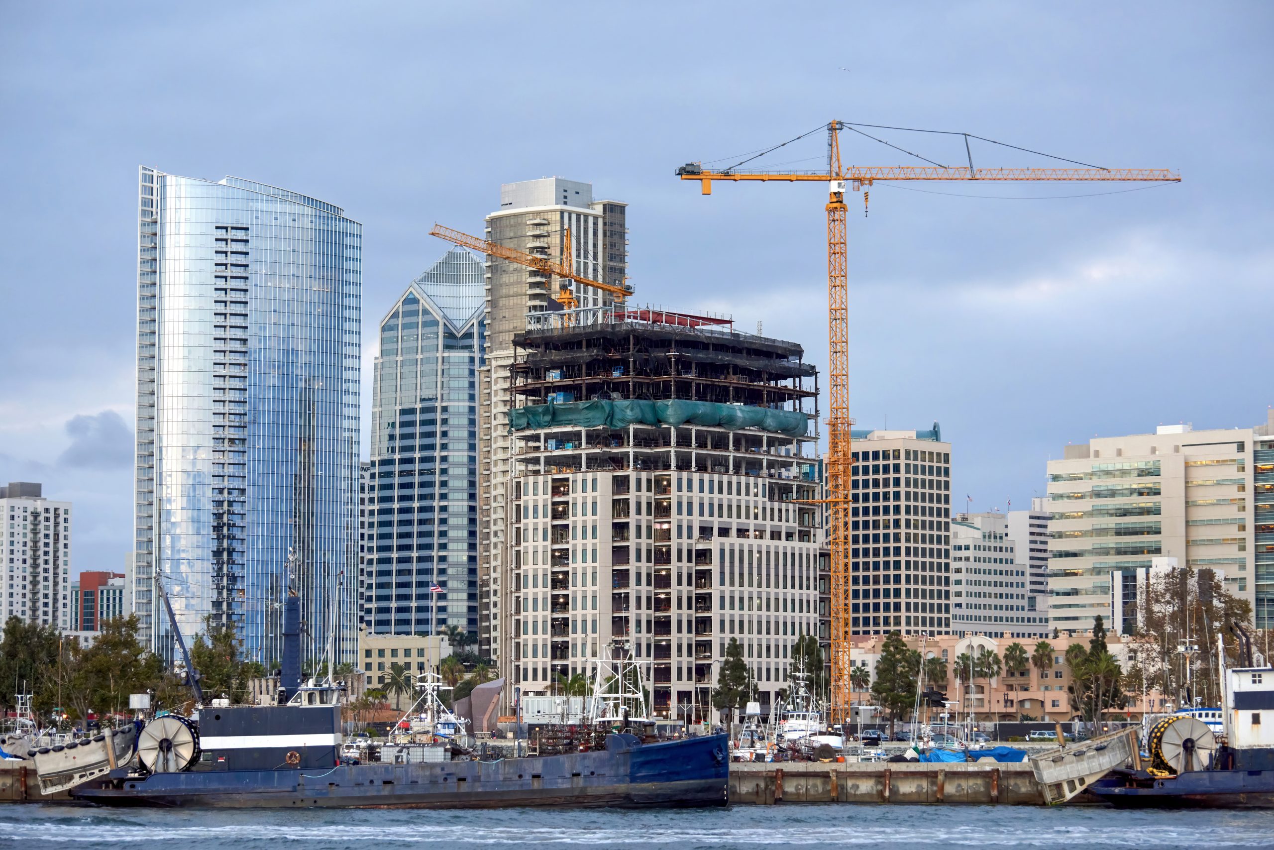 Construction works and high, modern buildings, yachts and two old moored boats on the foreground in San Diego, USA